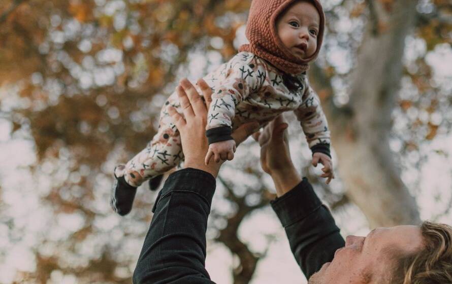 Parent lifting a bundled baby into the air outdoors in an autumn park, illustrating family life and parental responsibilities.