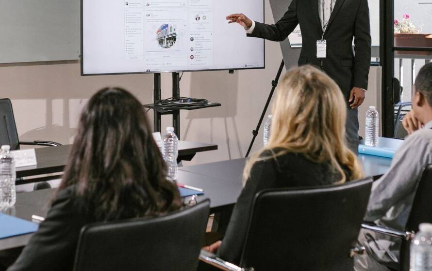 Instructor leading a classroom training session while participants listen and view a presentation screen, representing professional education and workforce development.
