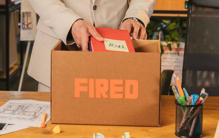 Employee packing personal files into a cardboard box marked “Fired” at an office desk, representing resignation, termination, and leaving a CBSA career.
