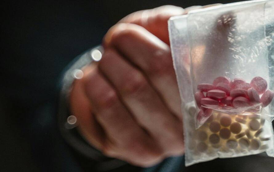 Close-up of a hand holding a small plastic bag containing pills, representing illegal drug trafficking and border enforcement investigations.