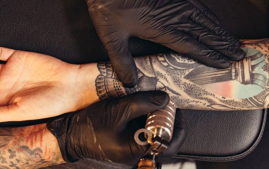 Tattoo artist working on a person's fully tattooed forearm, illustrating CBSA policies regarding visible tattoos, professional appearance, and applicant suitability.