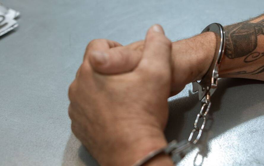Person in handcuffs seated at an interview table, representing criminal background assessments and security screening during the CBSA Border Services Officer recruitment process.