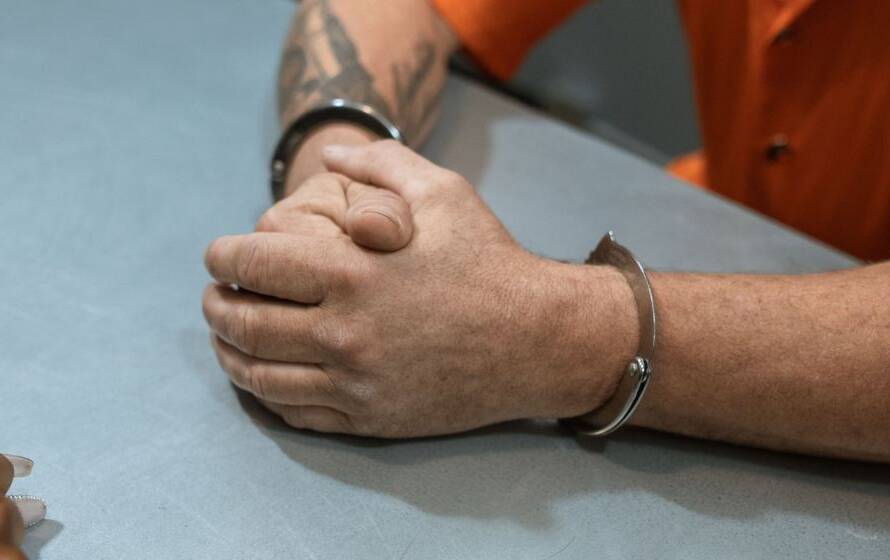 Individual in handcuffs seated across from an interviewer at a table, symbolizing disciplinary concerns, conduct investigations, and employee performance issues that may affect probationary employment status.